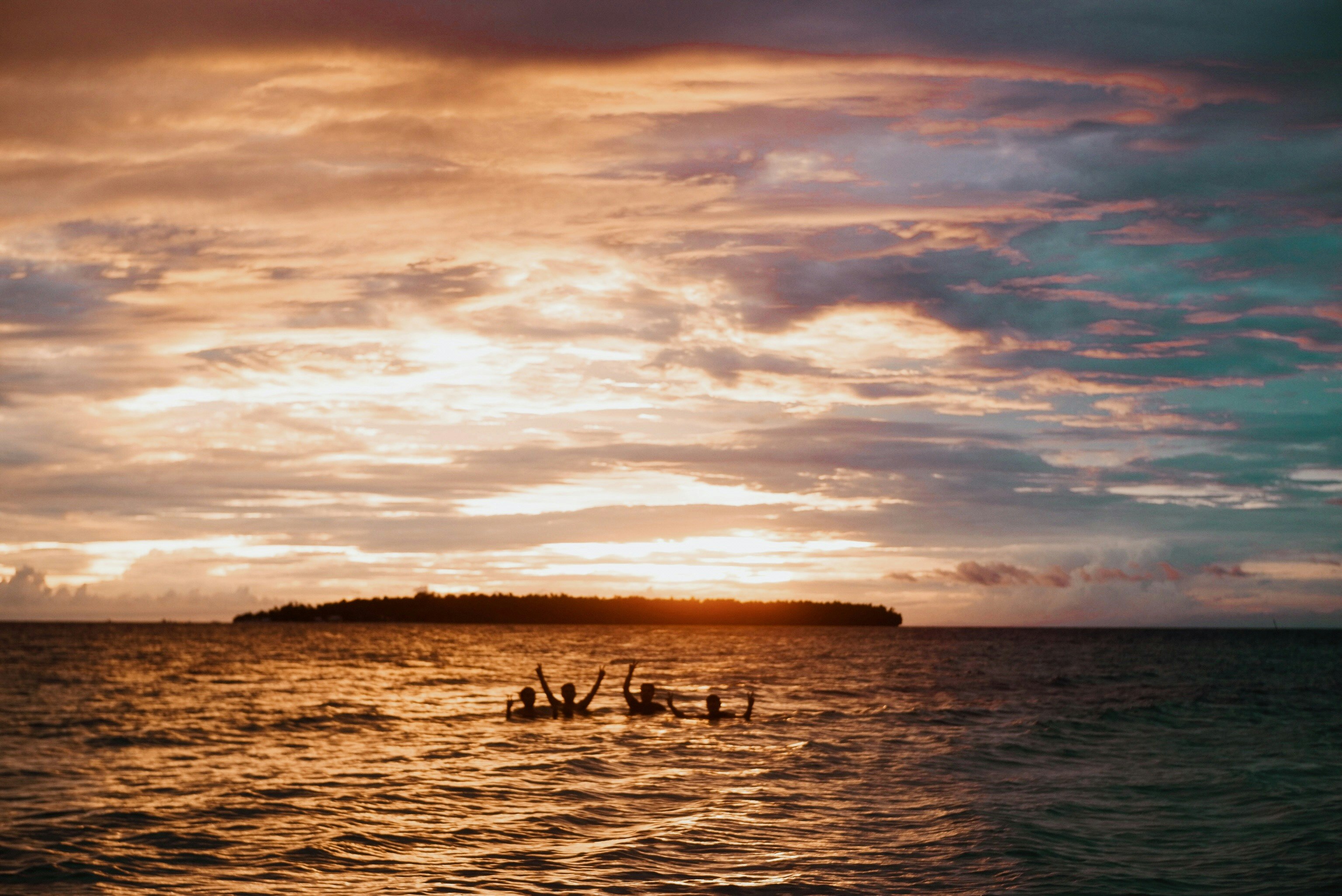 silhouette of people swimming on beach during golden hour